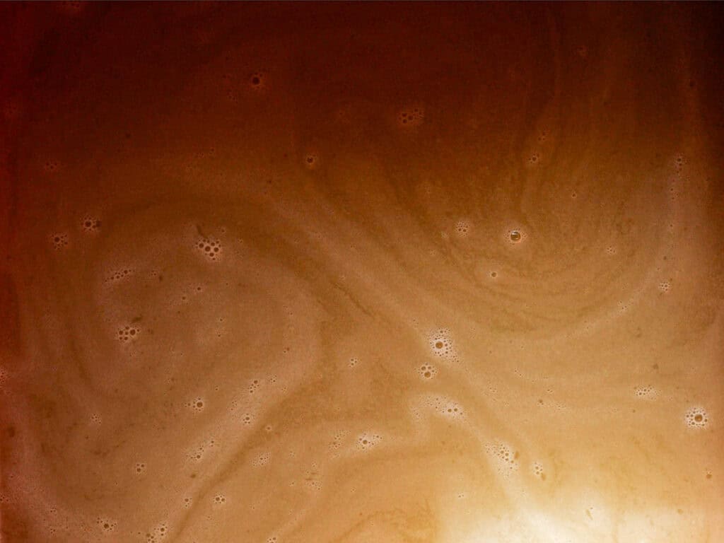 Swirling patterns of light and dark brown with small bubbles, resembling a foamy surface or liquid texture.